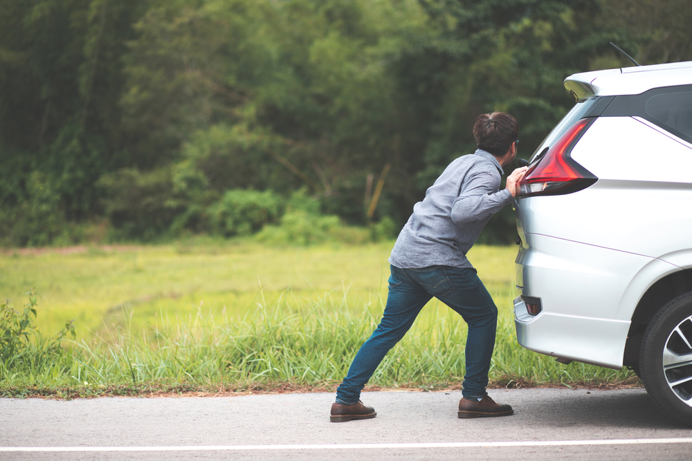 Man pushing broken car on street.