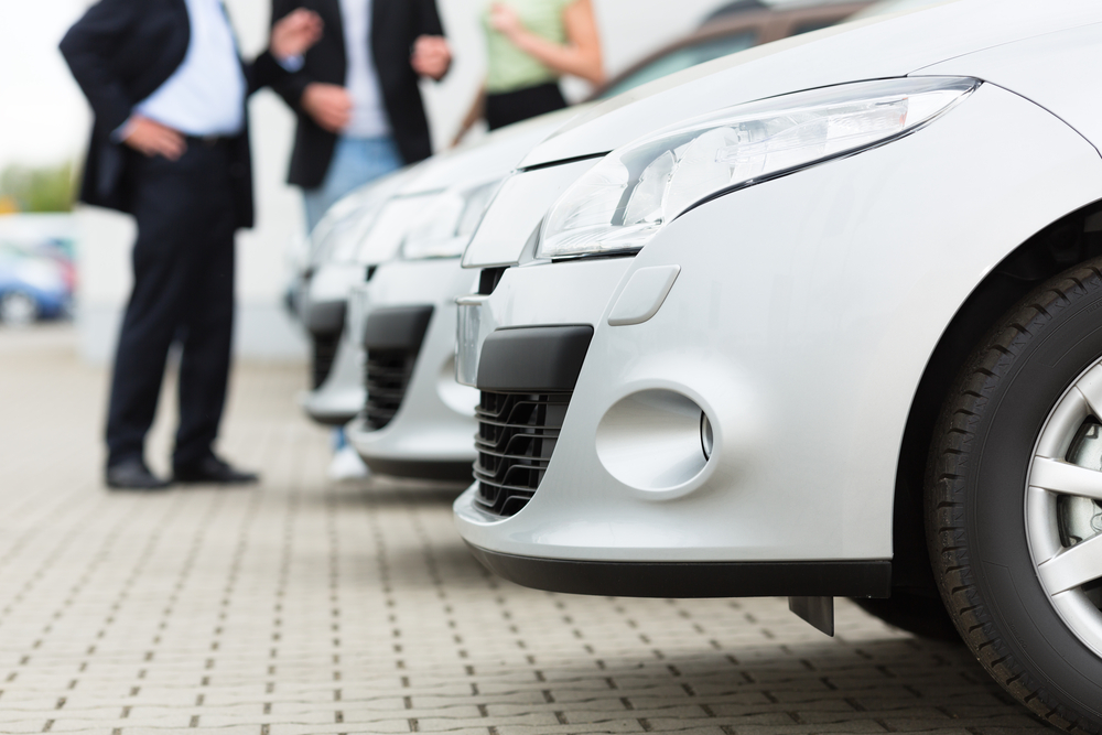 two men man and one woman stand behind a row of silver-metallic cars on a parking place